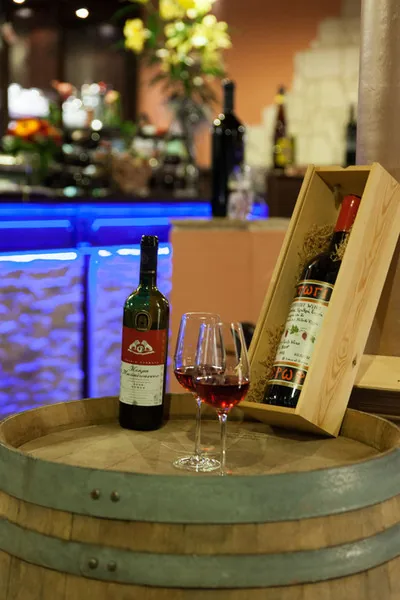 Weinfass mit Weinkiste und Weinglas vor der beleuchteten Theke