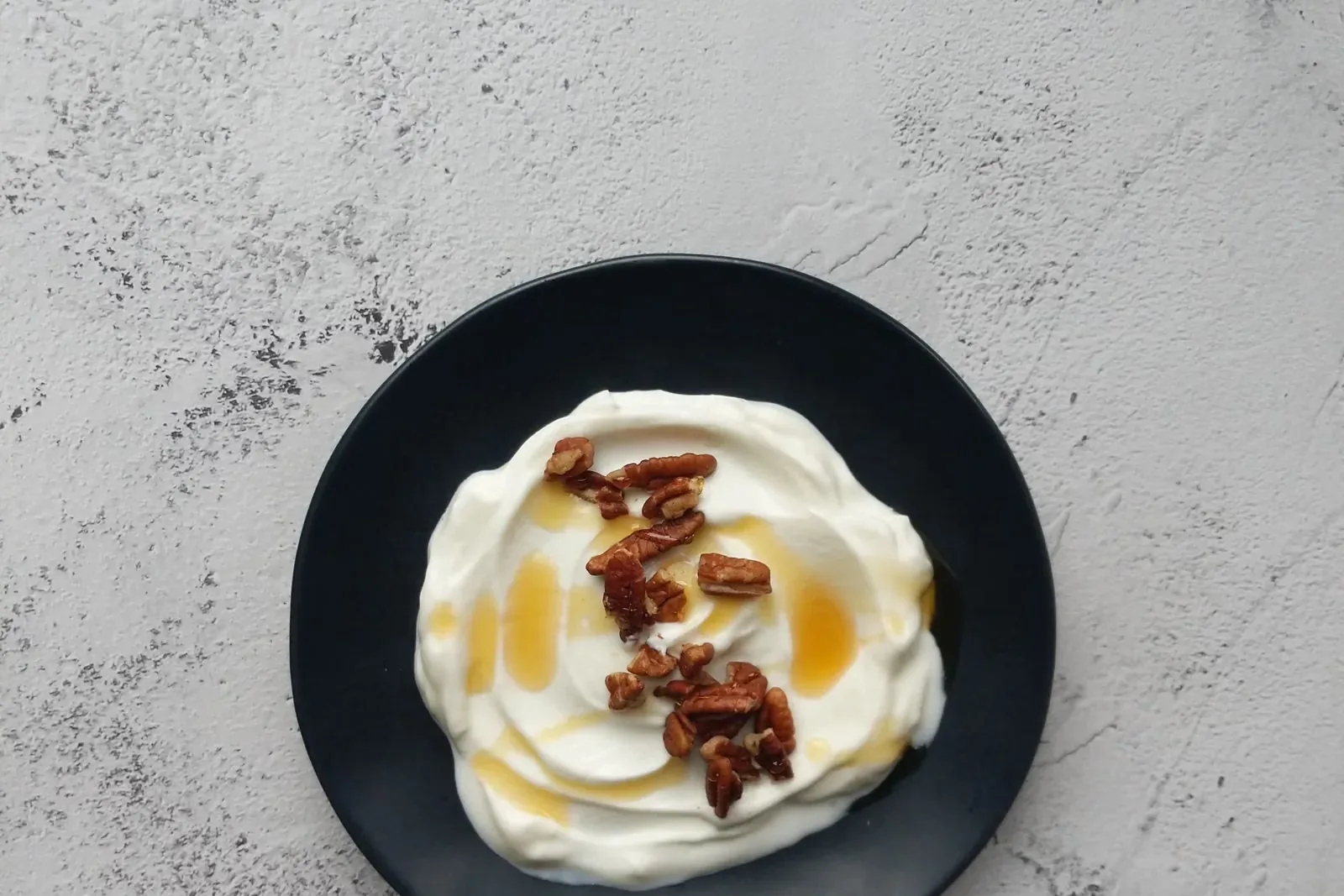 Joghurt mit Honig und Nüssen auf einem dunklen Teller, Stimmungsbild
